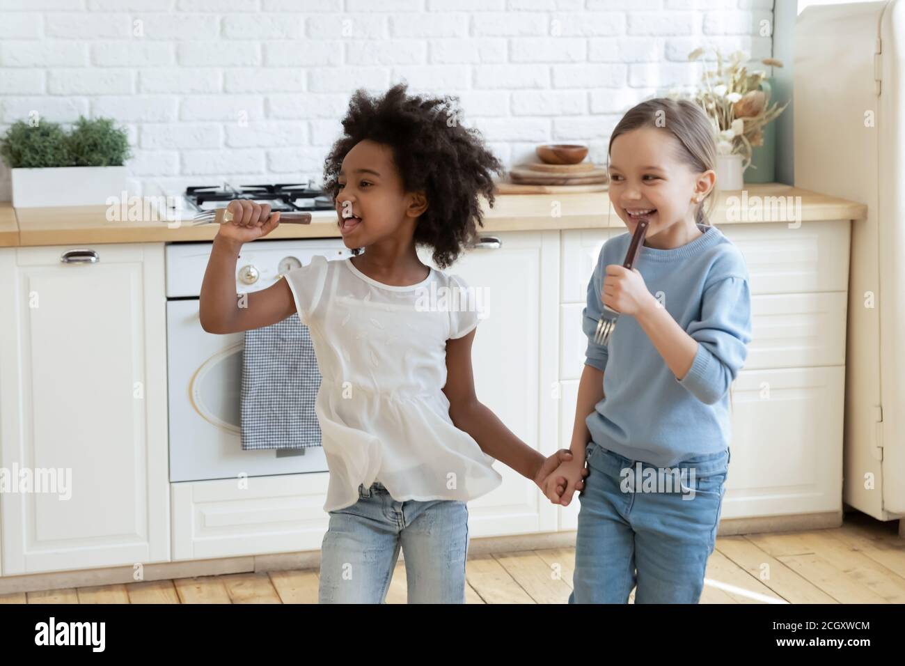 Little mixed race preschool kids enjoying singing songs in kitchen. Stock Photo