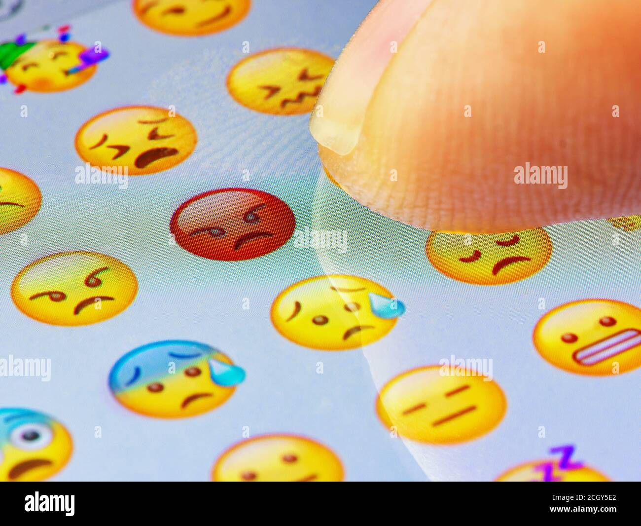 Macro finger touching angry emoji on a virtual keyboard Stock Photo