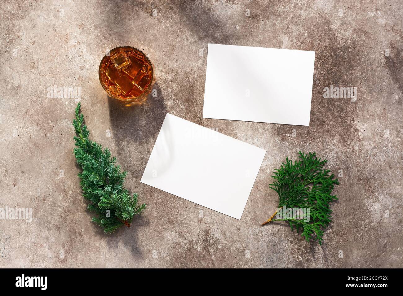 Whiskey glass with ice, blank white business card mockup, coniferous juniper and thuja branches. Male background. Alcohol industry template. Top view, Stock Photo