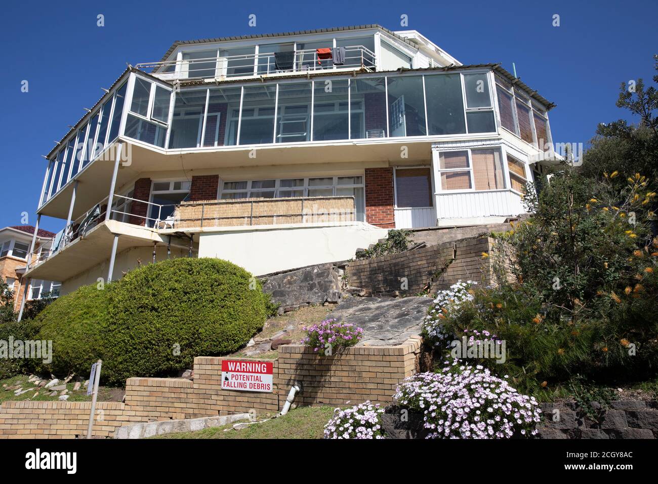 Large australian home with signs of settlement and subsidence is propped up with signs warning of falling debris,Whale beach Sydney,Australia Stock Photo