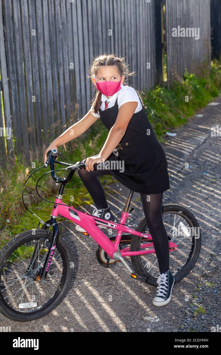 A ten year old schoolgirl in school uniform sitting on her pink bicycle and wearing a pink face mask. Stock Photo