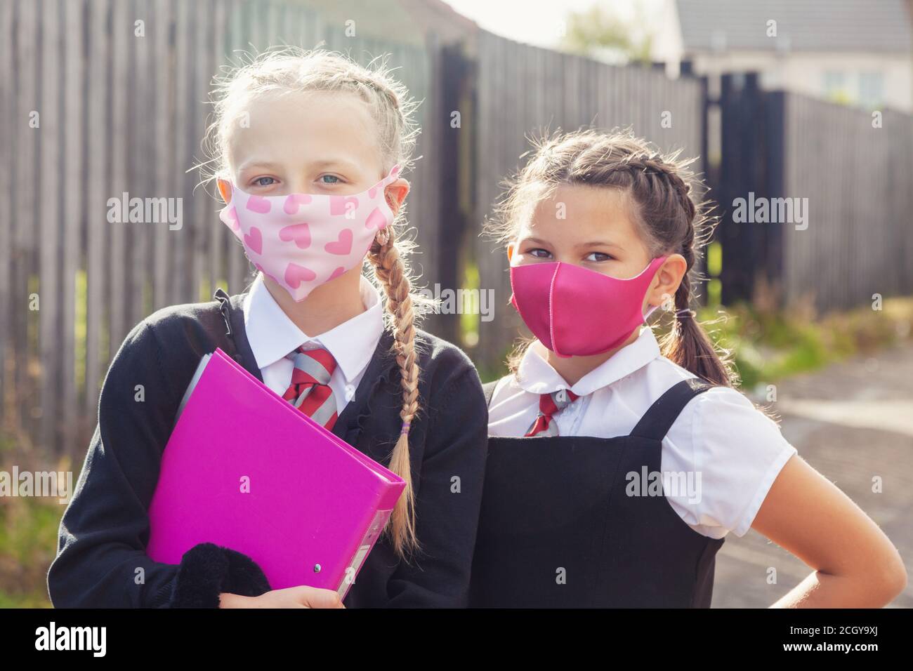 Two ten year old schoolgirls in school uniforms and wearing face masks. Stock Photo