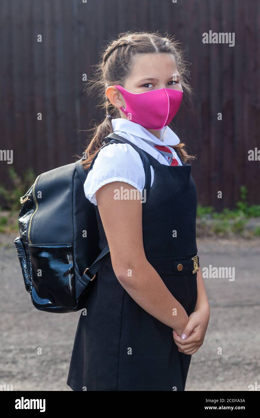 A 10 year old schoolgirl in school uniform and wearing a pink face mask Stock Photo