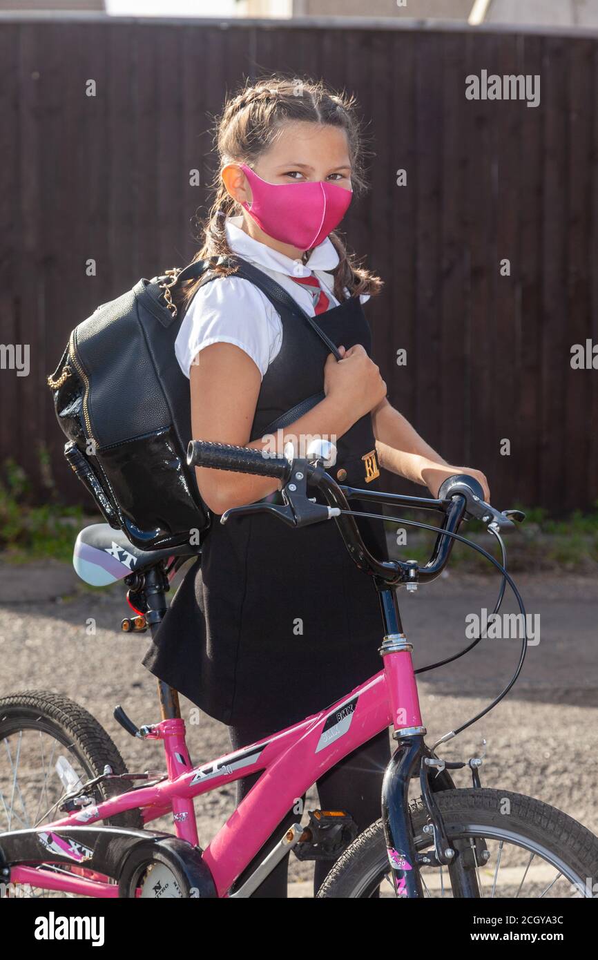 A 10 year old schoolgirl in school uniform wearing a pink face mask standing with her pink bike Stock Photo