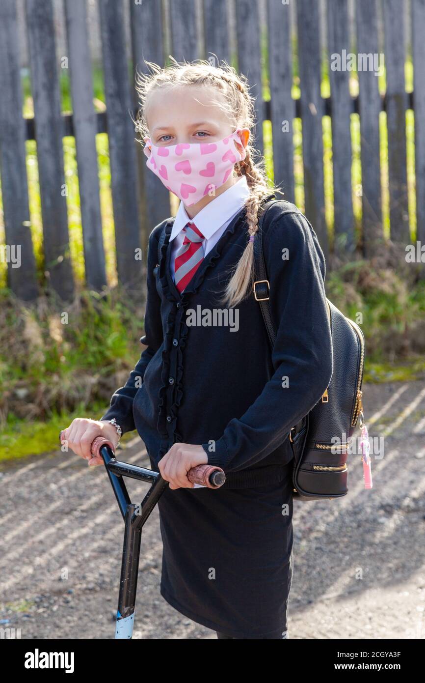 A 10 year old schoolgirl wearing a face mask and holding the handlebars of her scooter Stock Photo