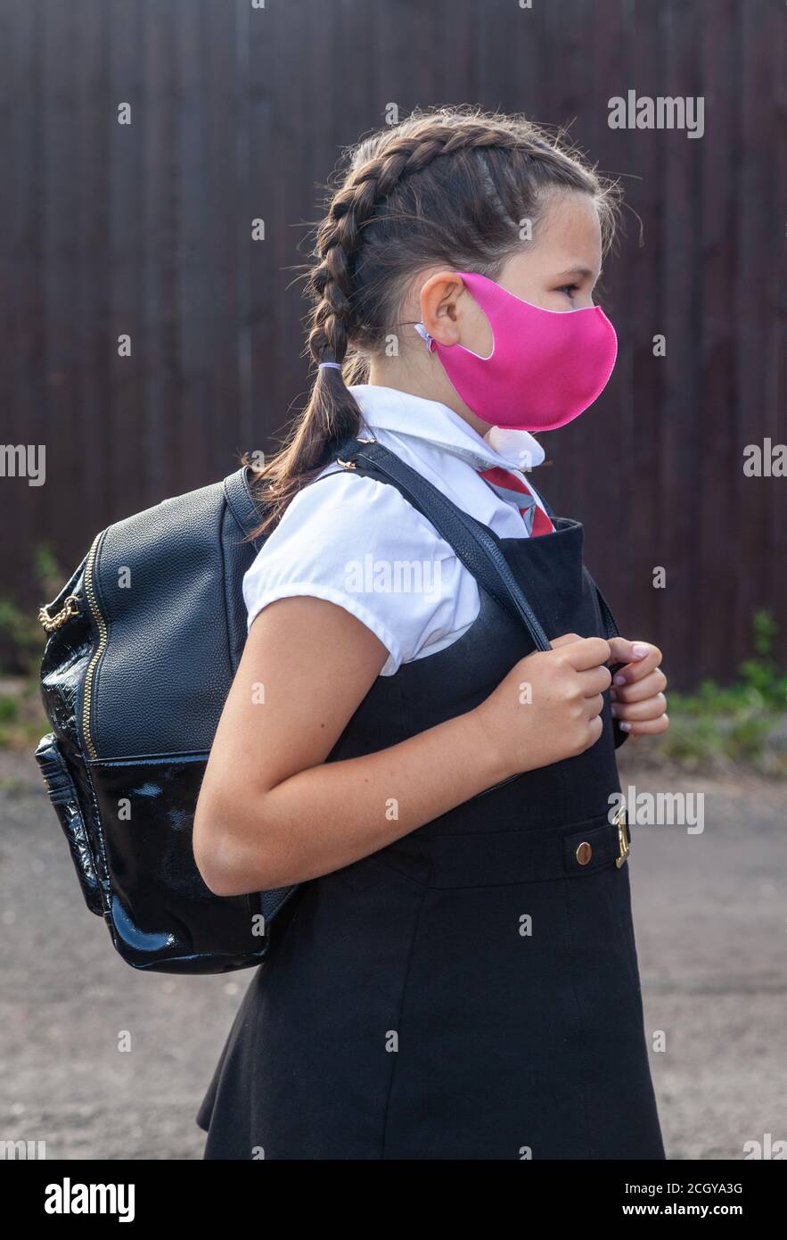 A 10 year old schoolgirl in school uniform and wearing a pink face mask Stock Photo