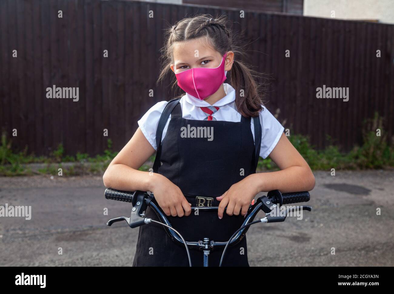 A ten year old schoolgirl standing with her hands on her bike wearing a face mask. Stock Photo