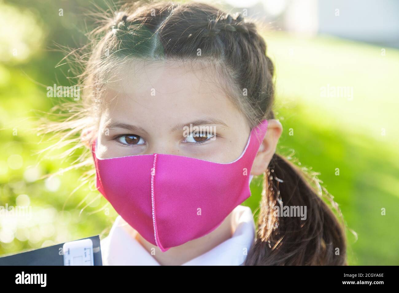 Close up of the face of a 10 year old girl with her hair in braids and wearing a pink face mask. Stock Photo