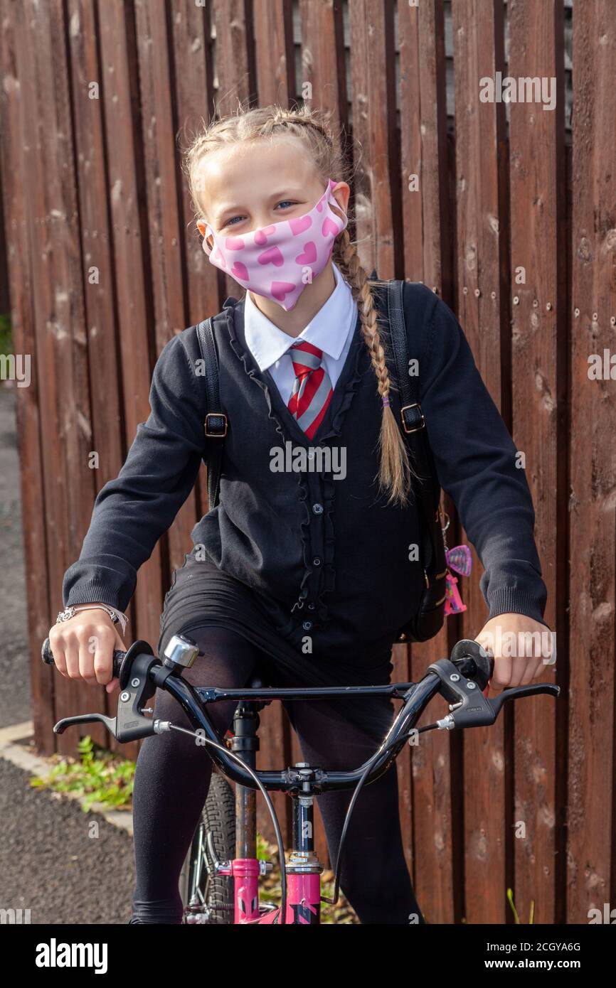 A 10 year old schoolgirl in school uniform sitting on her bike and wearing a face mask. Stock Photo