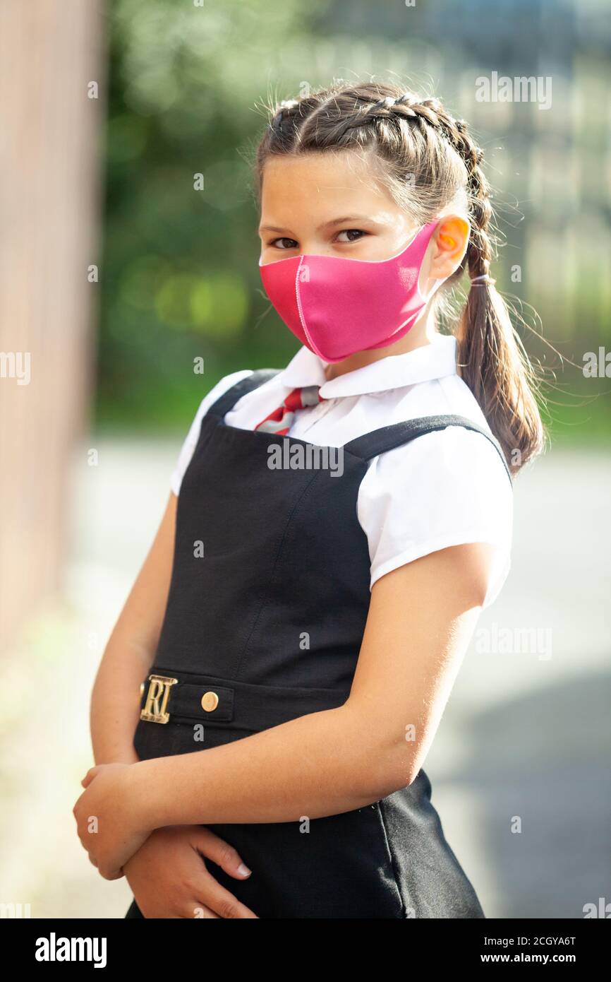 A ten year old schoolgirl in a school uniform with her hair in braids and wearing a pink face mask. Stock Photo