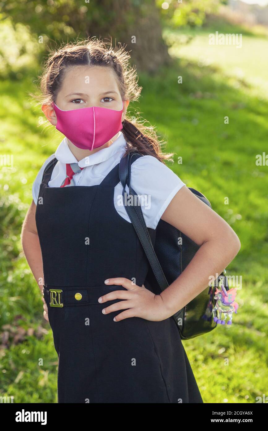 A ten year old schoolgirl in a school uniform with her hair in braids and wearing a pink face mask. Stock Photo