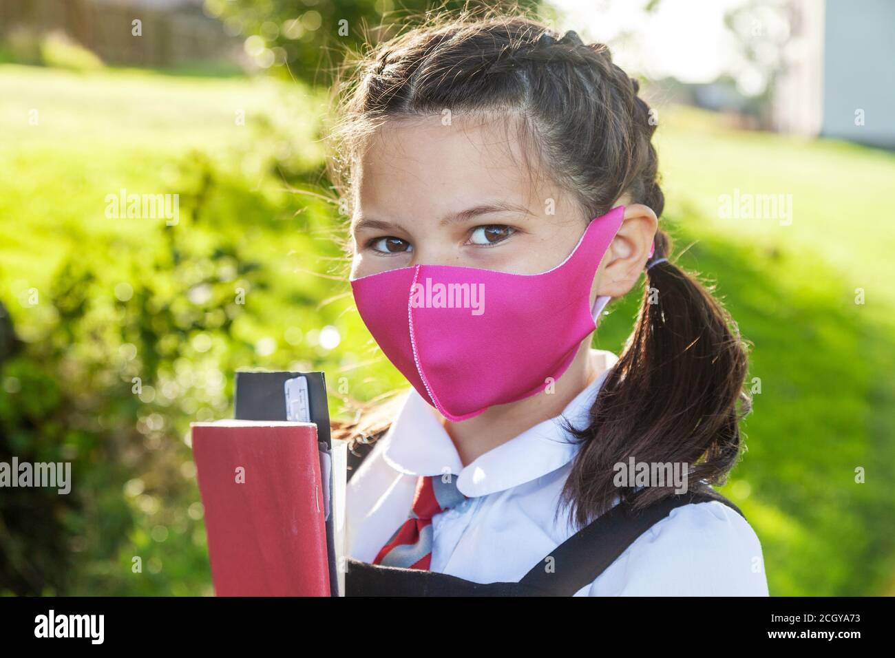 Close up of the face of a 10 year old girl with her hair in braids and wearing a pink face mask. Stock Photo