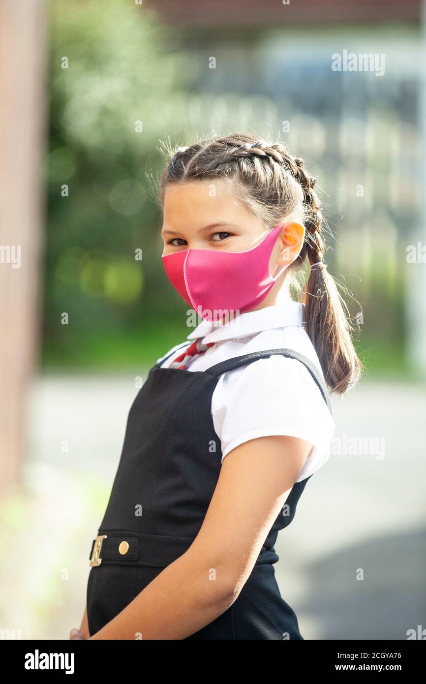 A ten year old schoolgirl in a school uniform with her hair in braids and wearing a pink face mask. Stock Photo