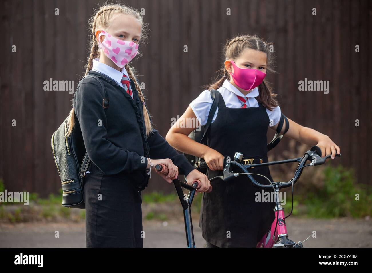 Two 10 year old schoolgirls in school uniform with their scooter and bike and wearing face masks Stock Photo