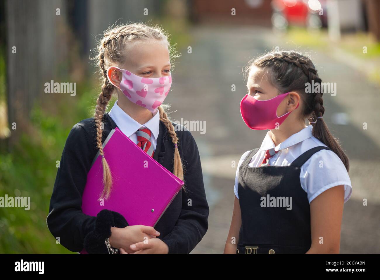 Two 10 year old schoolgirls in school uniform and face masks standing outside looking at each other Stock Photo