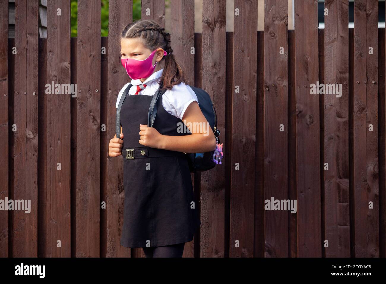 A 10 year old schoolgirl wearing a school uniform and pink face mask and looking away. Stock Photo