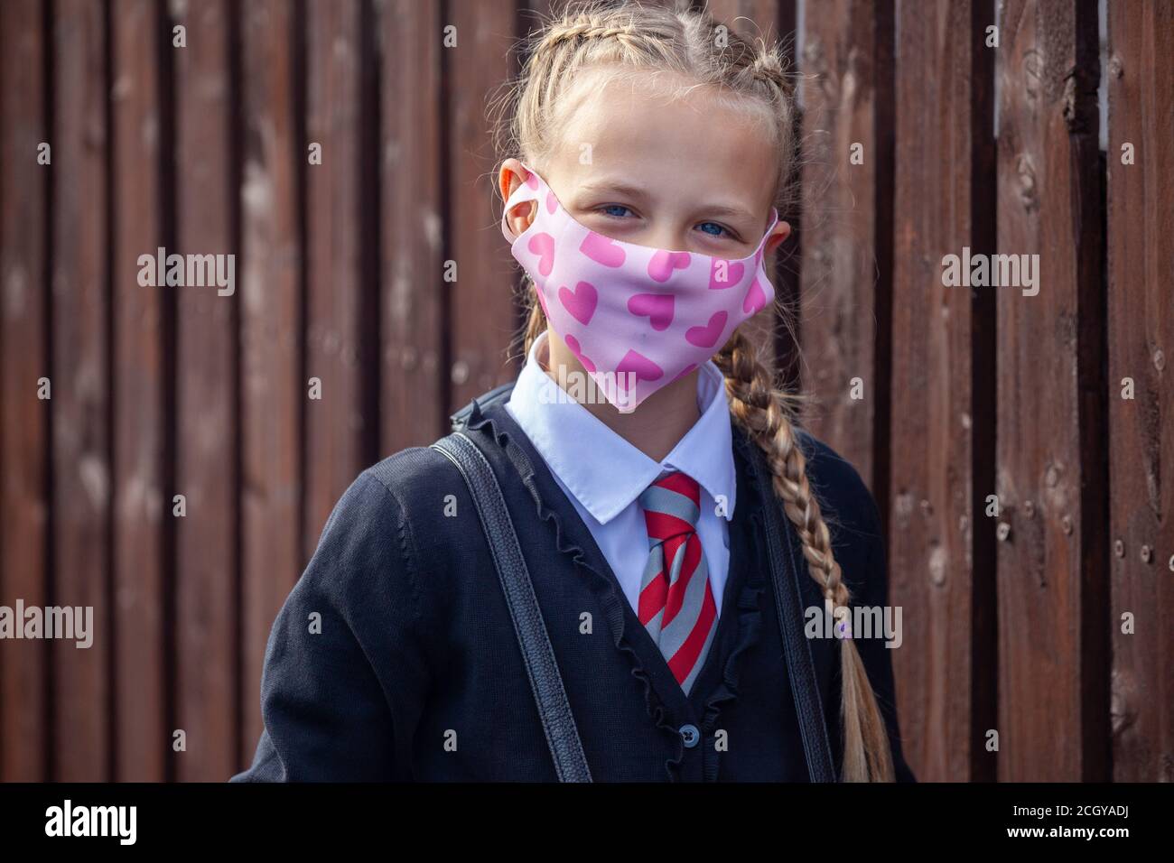 A ten year old schoolgirl wearing a school uniform and pink face mask with hearts looking at camera Stock Photo