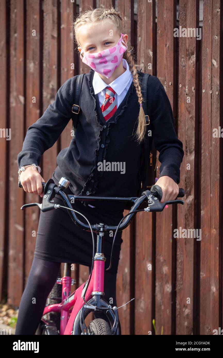 A ten year old schoolgirl wearing a school uniform and pink face mask and sitting on her bike looking at camera Stock Photo