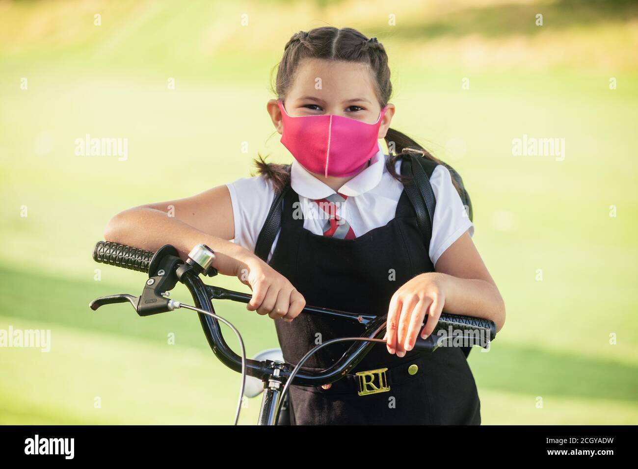 A ten year old schoolgirl standing with her hands on her bike wearing a face mask. Stock Photo