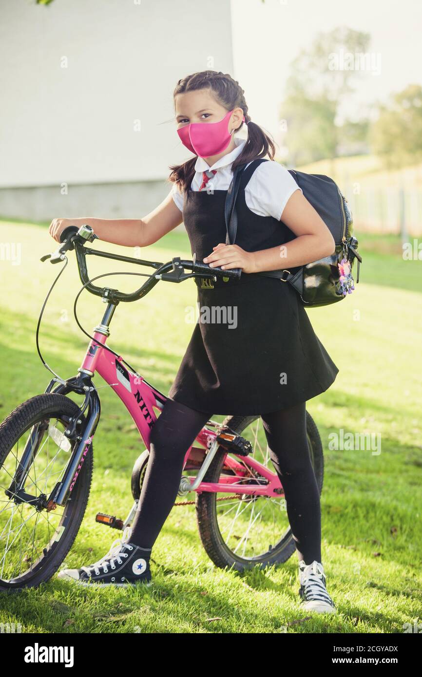 A 10 year old schoolgirl wearing a school uniform and face mask and standing next to her bicycle Stock Photo