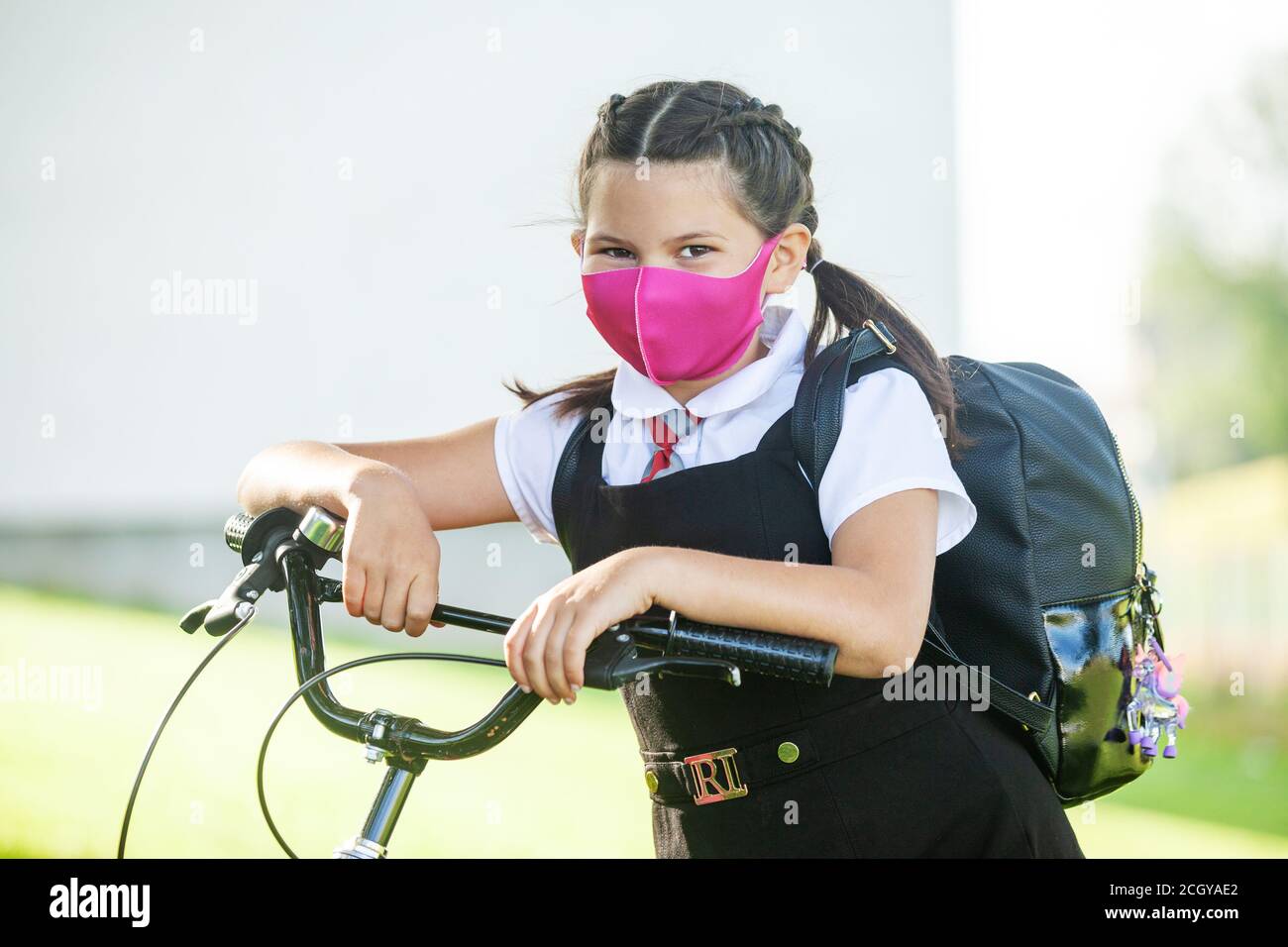 A ten year old schoolgirl standing with her hands on her bike wearing a face mask. Stock Photo