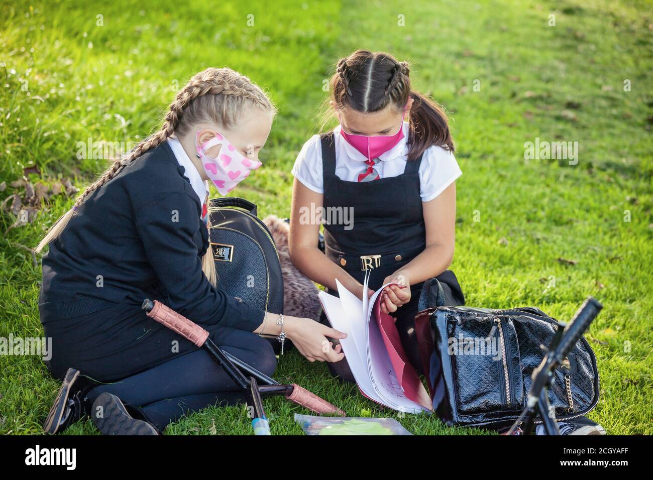 Two young school children sitting down outside wearing face masks and looking at homework, Scotland, UK Stock Photo