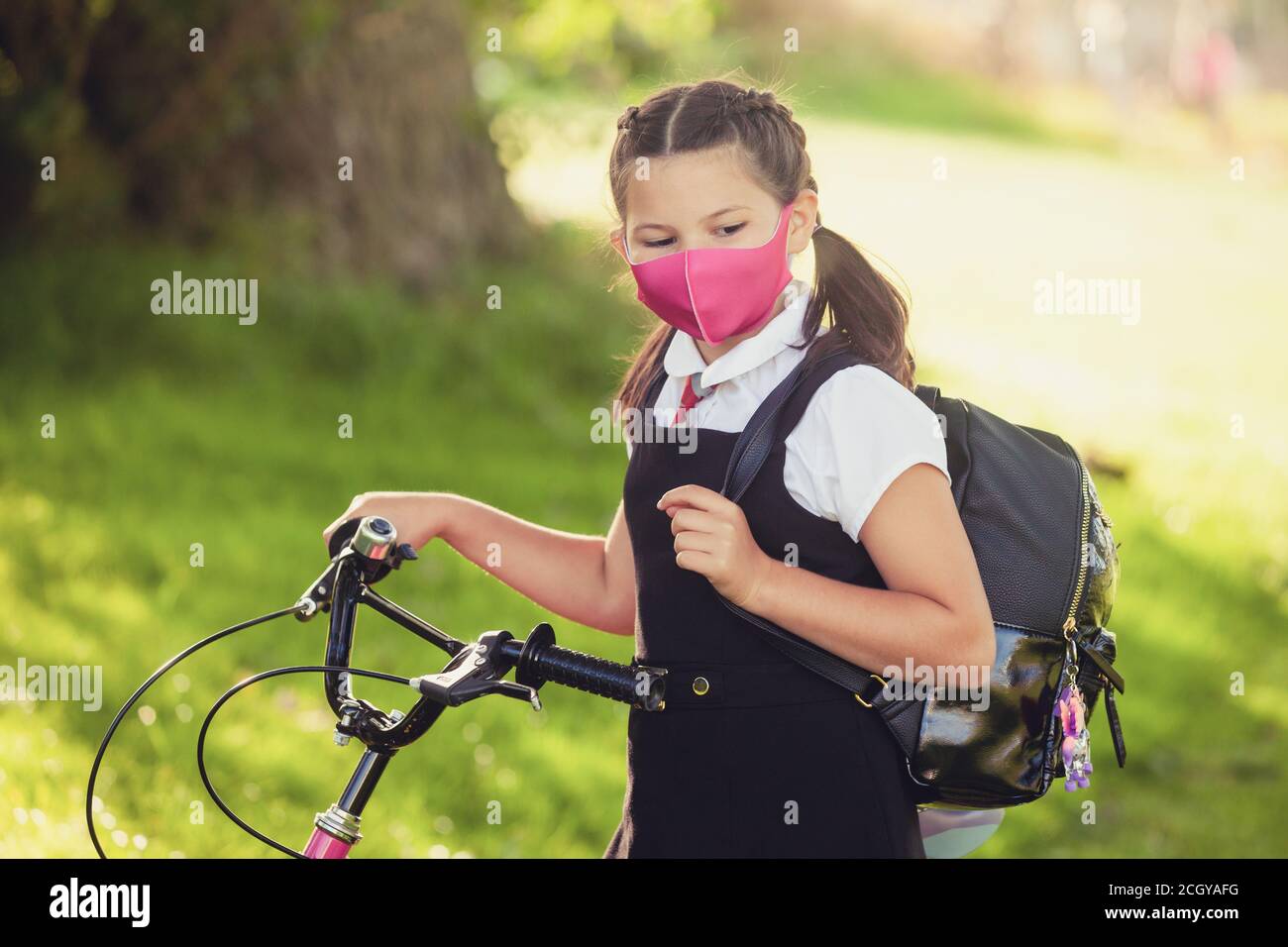 A ten year old schoolgirl standing with her hand on her bike wearing a face mask. Stock Photo