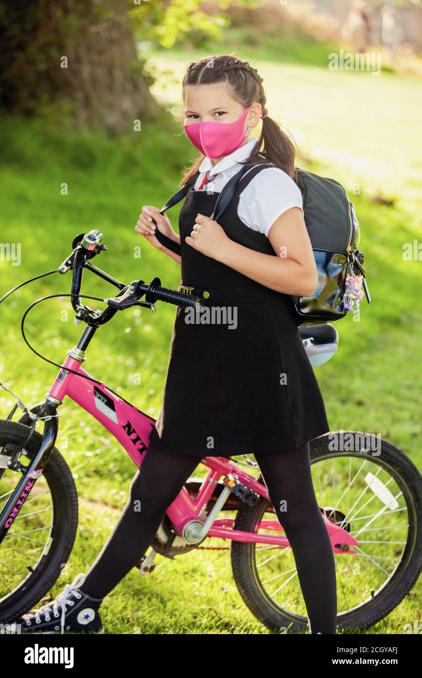 A 10 year old schoolgirl wearing a school uniform and face mask and standing next to her bicycle Stock Photo