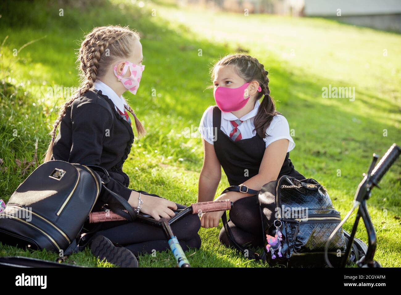 Two young schoolchildren sitting outside chatting and wearing face masks, Scotland, UK Stock