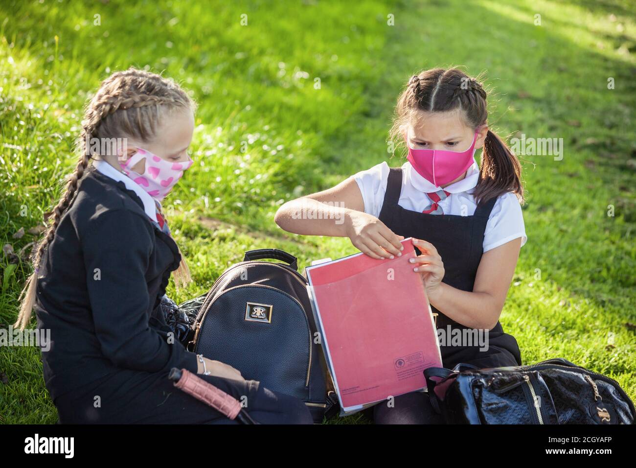 Two young school children sitting down outside wearing face masks and looking at homework, Scotland, UK Stock Photo