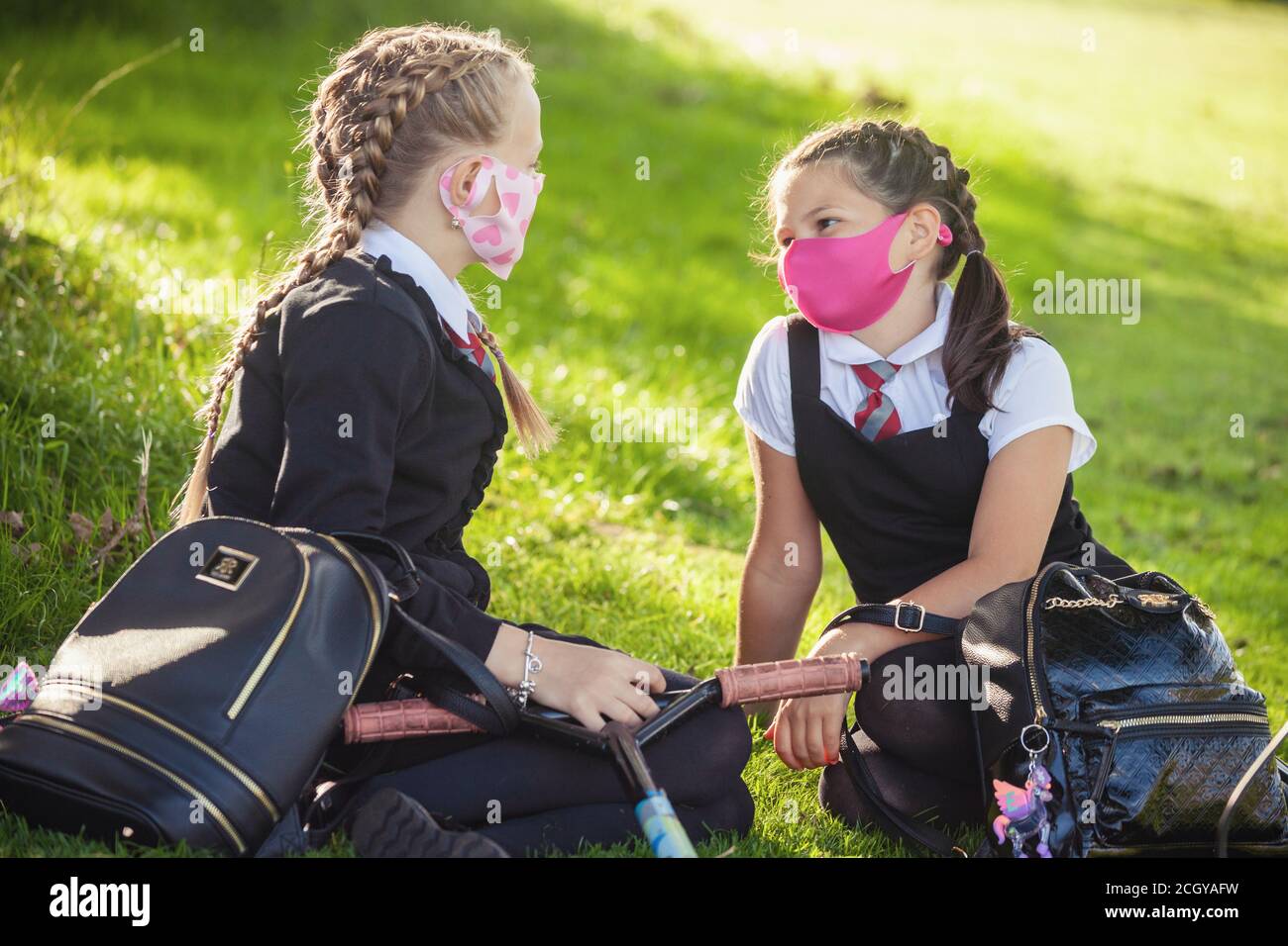 Two young schoolchildren sitting outside chatting and wearing face masks, Scotland, UK Stock Photo