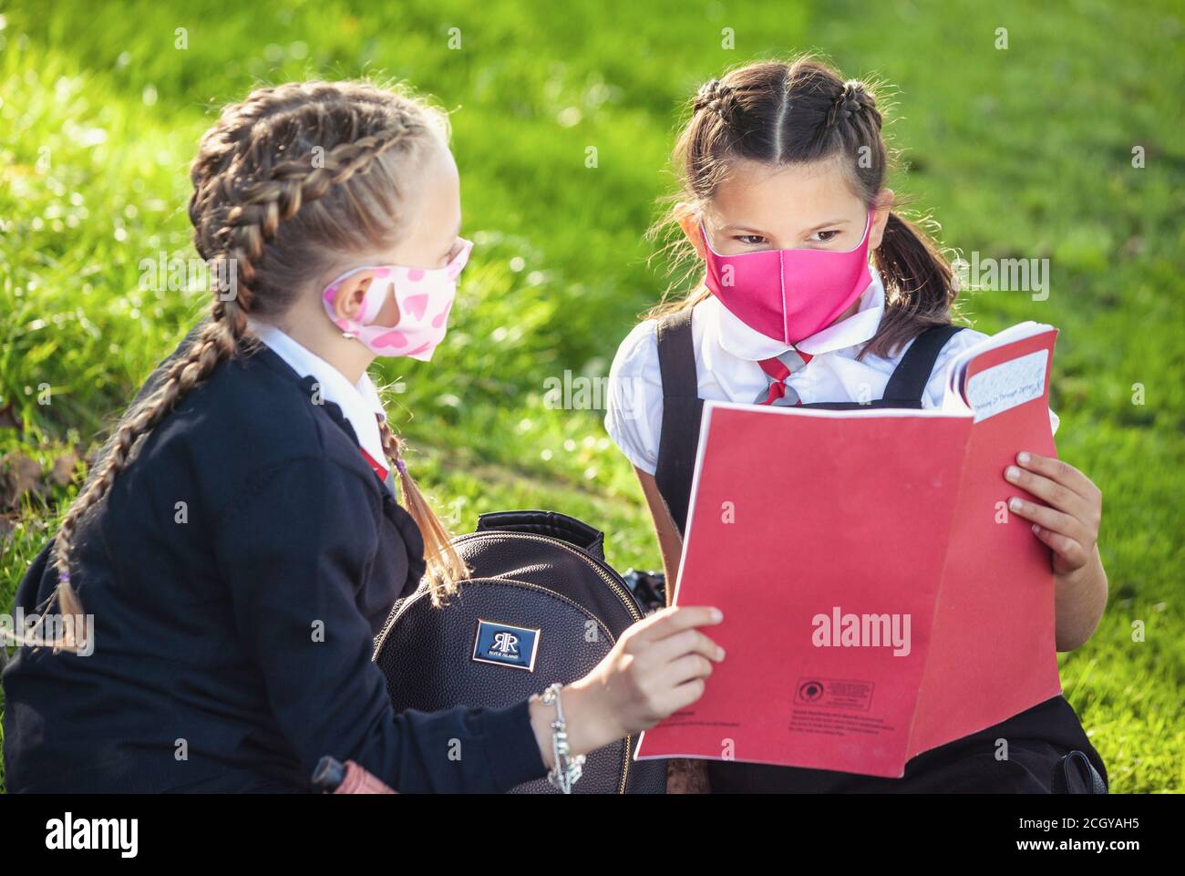 Two young school children sitting down outside wearing face masks and looking at homework, Scotland, UK Stock Photo