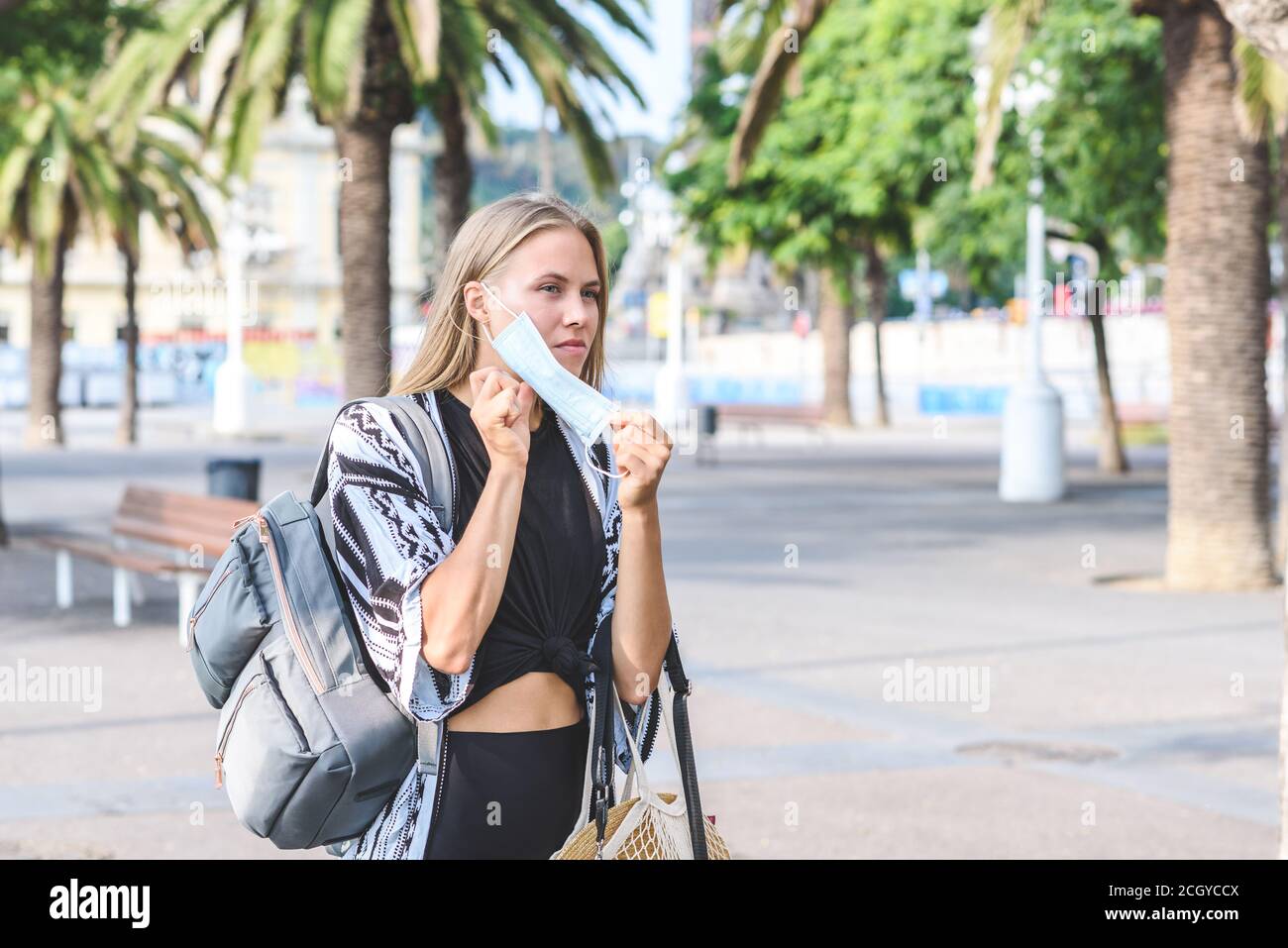 blonde caucasian young woman putting on a protective blue surgical mas in the street Stock Photo