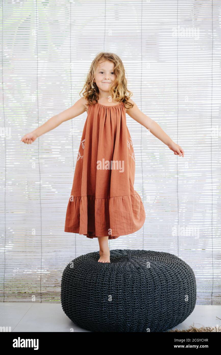 Happy little girl in long dress standing on a high black wicker