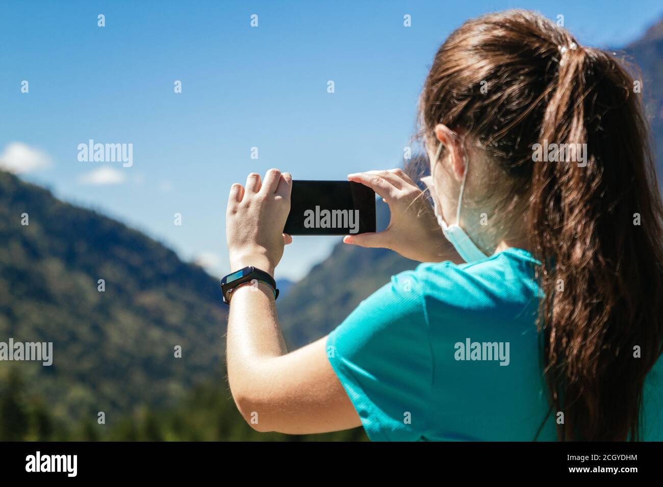 Stock photo of a woman from behind with face mask taking a photo of a beautiful landscape with her phone Stock Photo