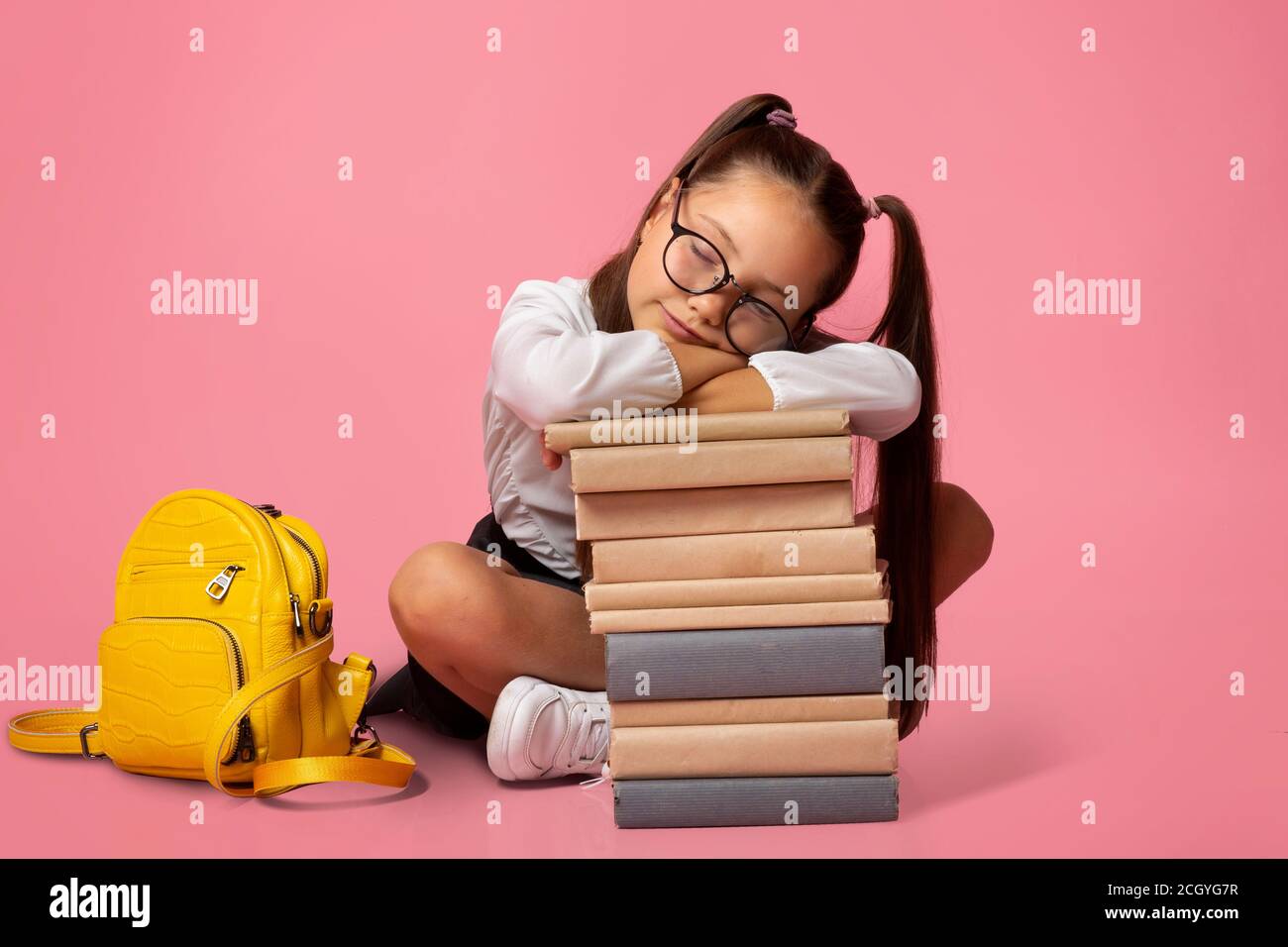 Sad and tired concept. Girl in glasses in uniform with backpack sleeps on stack of books Stock Photo