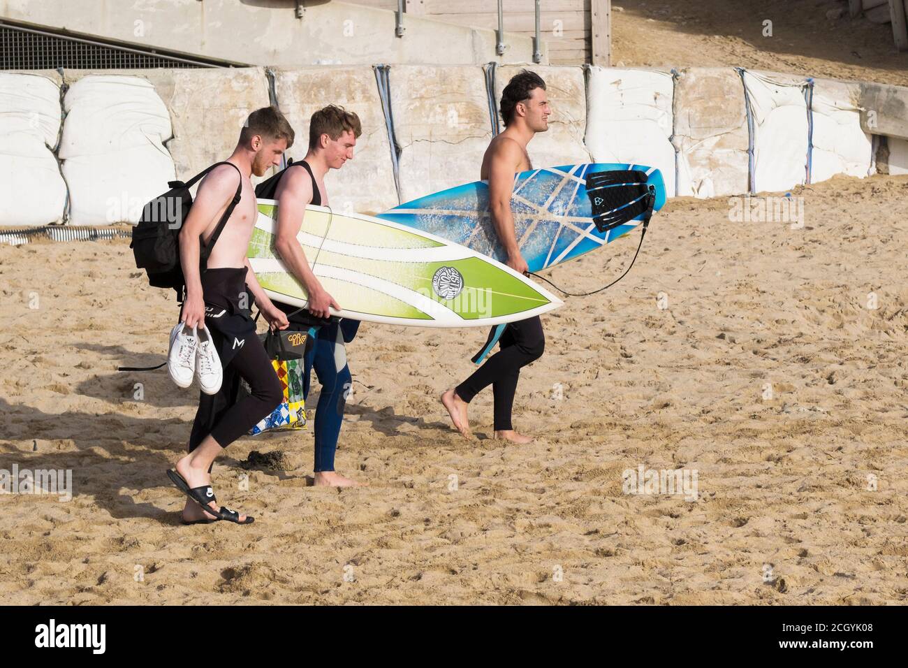 Three surfers carrying their surfboards and walking across Fistral Beach in Newquay in Cornwall. Stock Photo