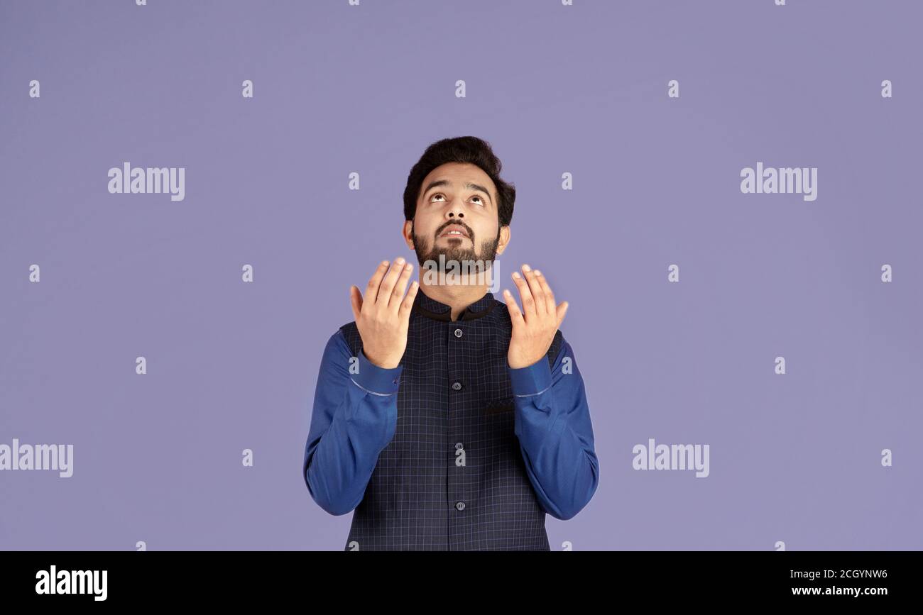 Religious Indian guy praying to God, asking for redemption on violet background Stock Photo