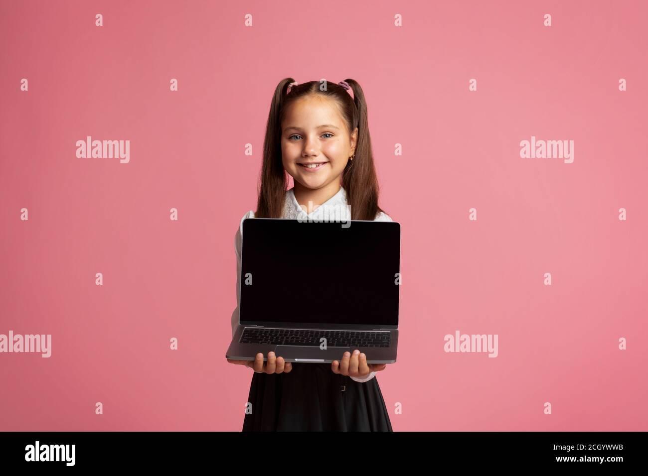 Remote education during quarantine. Smiling girl in school uniform holding laptop Stock Photo