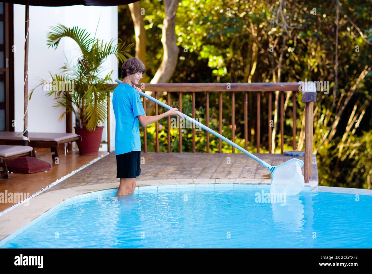 Boy cleaning swimming pool. Maintenance and service for outdoor pool. Teenager after school job and house help. Teen student picking foliage leaf out Stock Photo