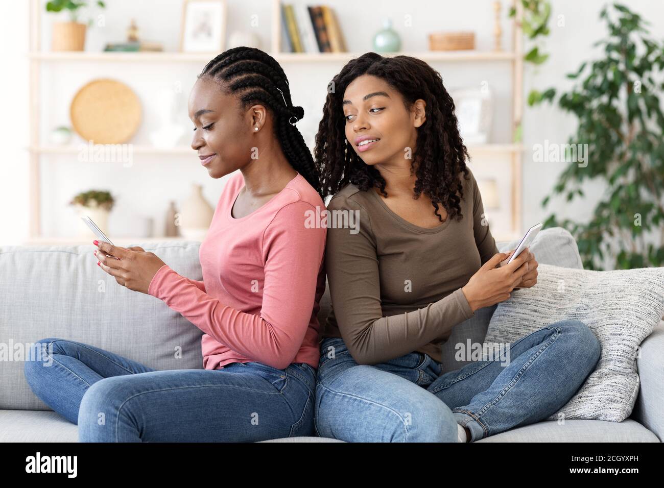Young black women sitting back to back, using smartphones Stock Photo