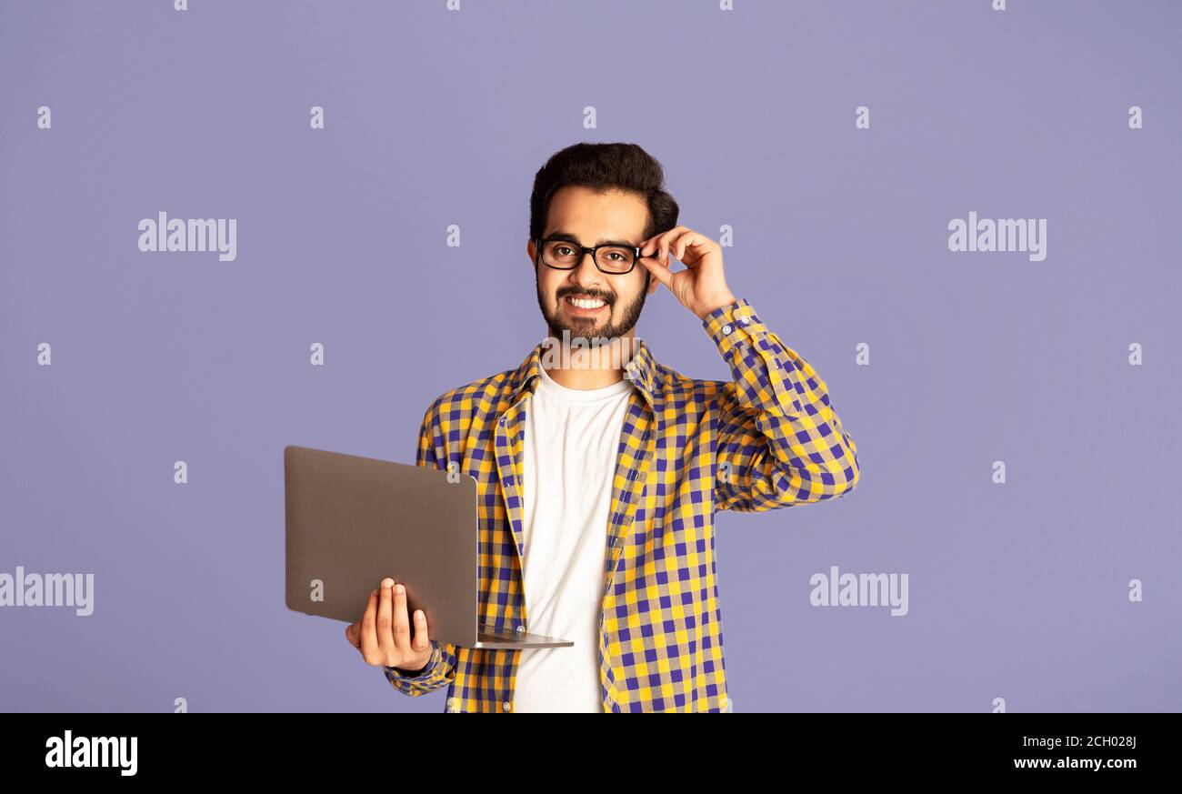 Happy Indian guy in glasses using laptop computer for distance work or