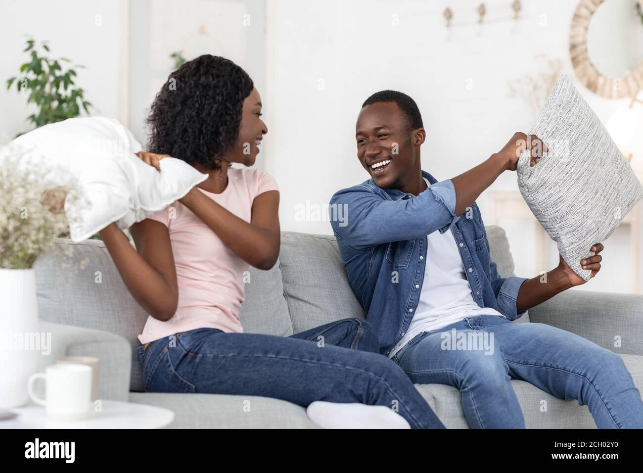 Cheerful loving black couple fighting with pillows in living room Stock Photo