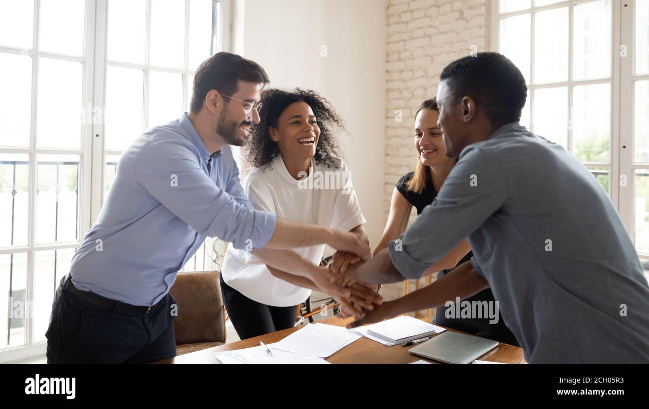 Overjoyed multicultural coworkers stack hands engaged in teambuilding Stock Photo