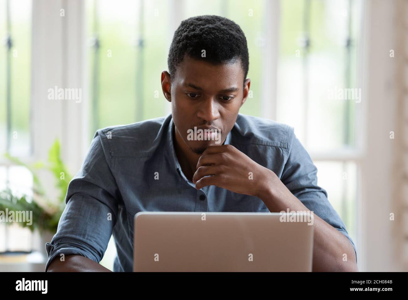 Pensive biracial male employee work on laptop thinking Stock Photo