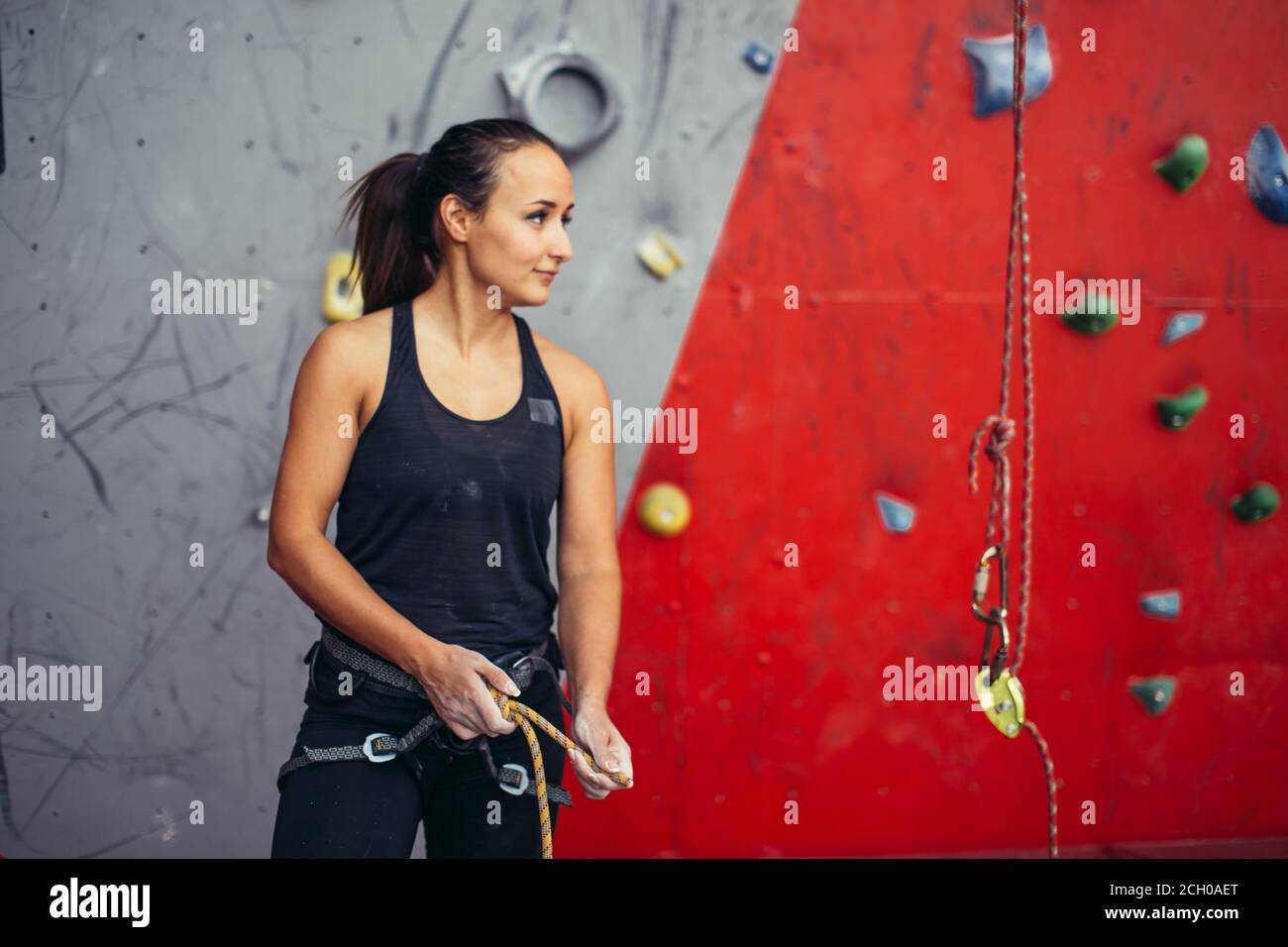 Athletic female climber in safety harness tying rope in eight knot and