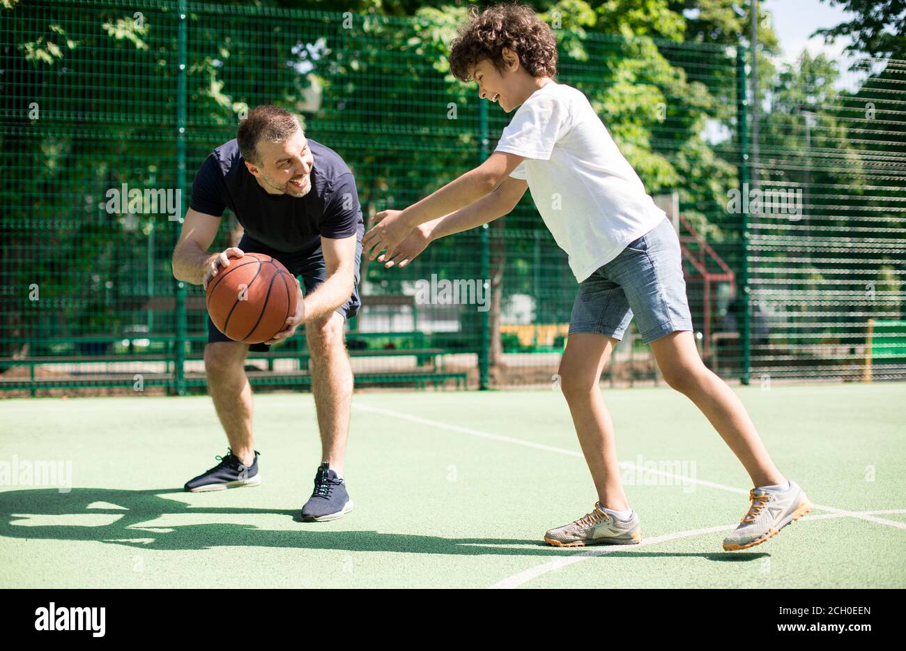 Cheerful man teaching boy how to play basketball Stock Photo Alamy