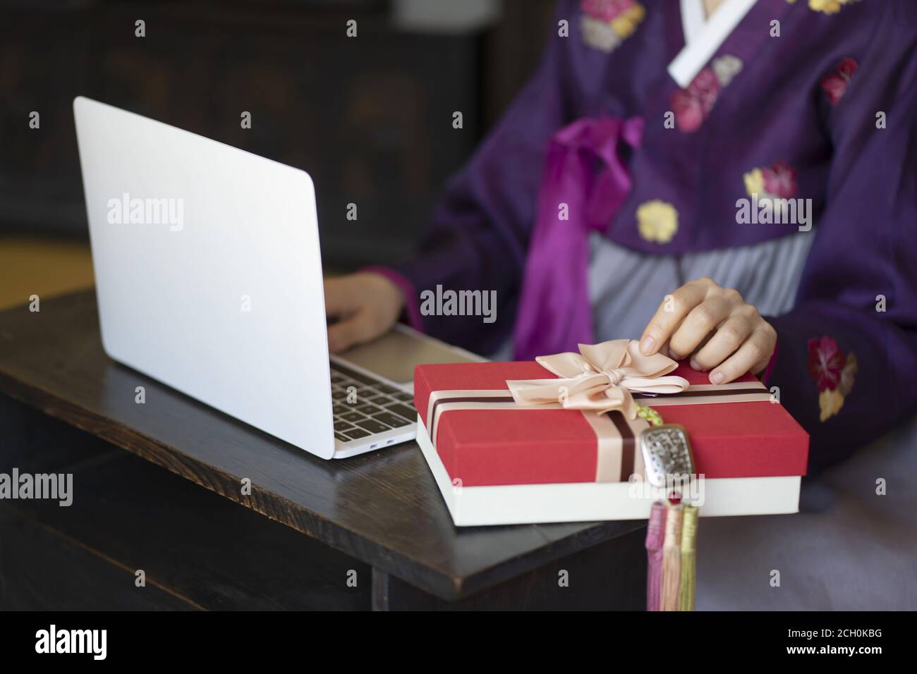 Woman in Korean traditional clothes using laptop with gift box Stock Photo