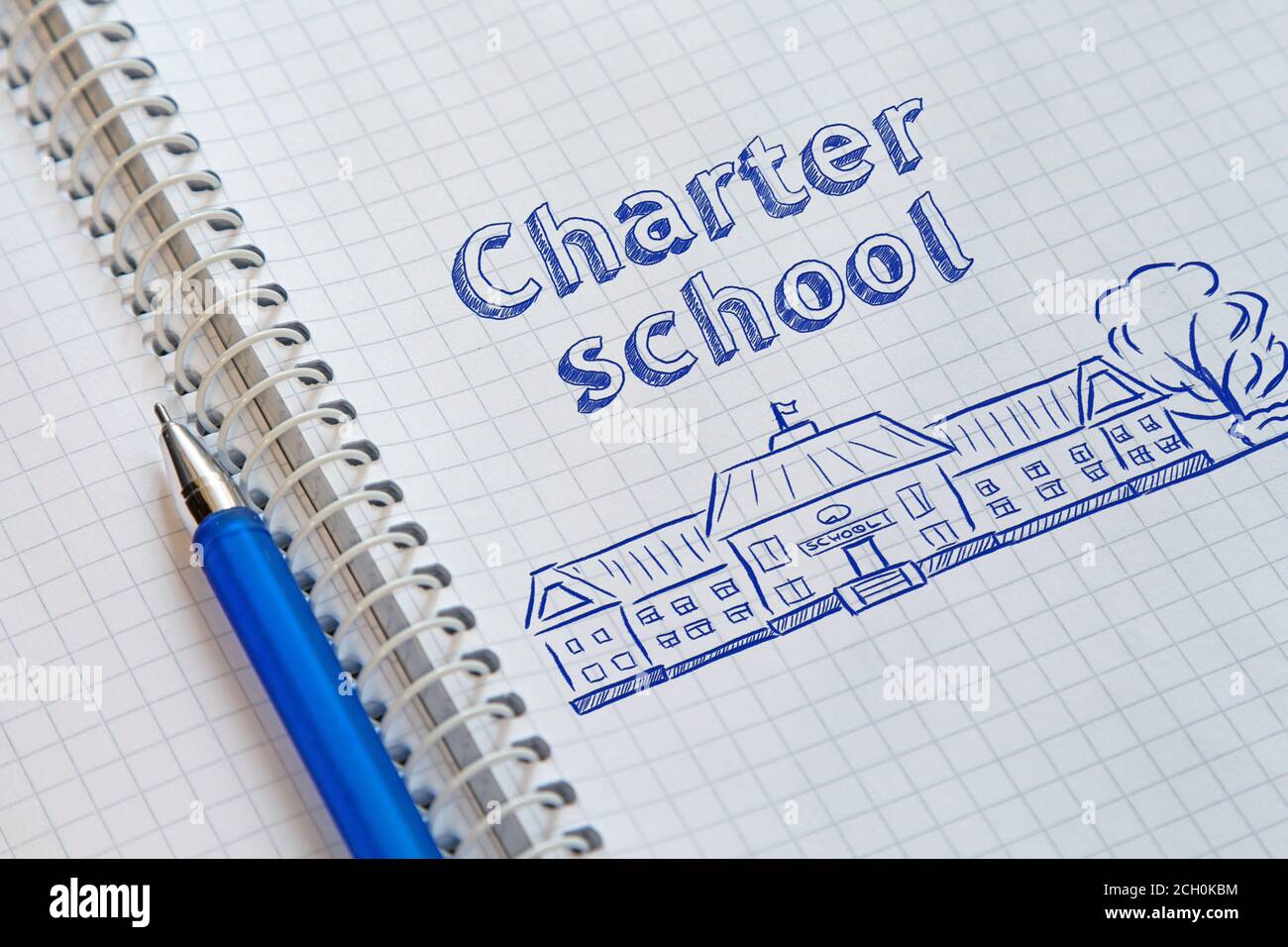 Notebook with a spiral in a cage and blue pen on it. On the left page drawn the school and lettering Charter school Stock Photo