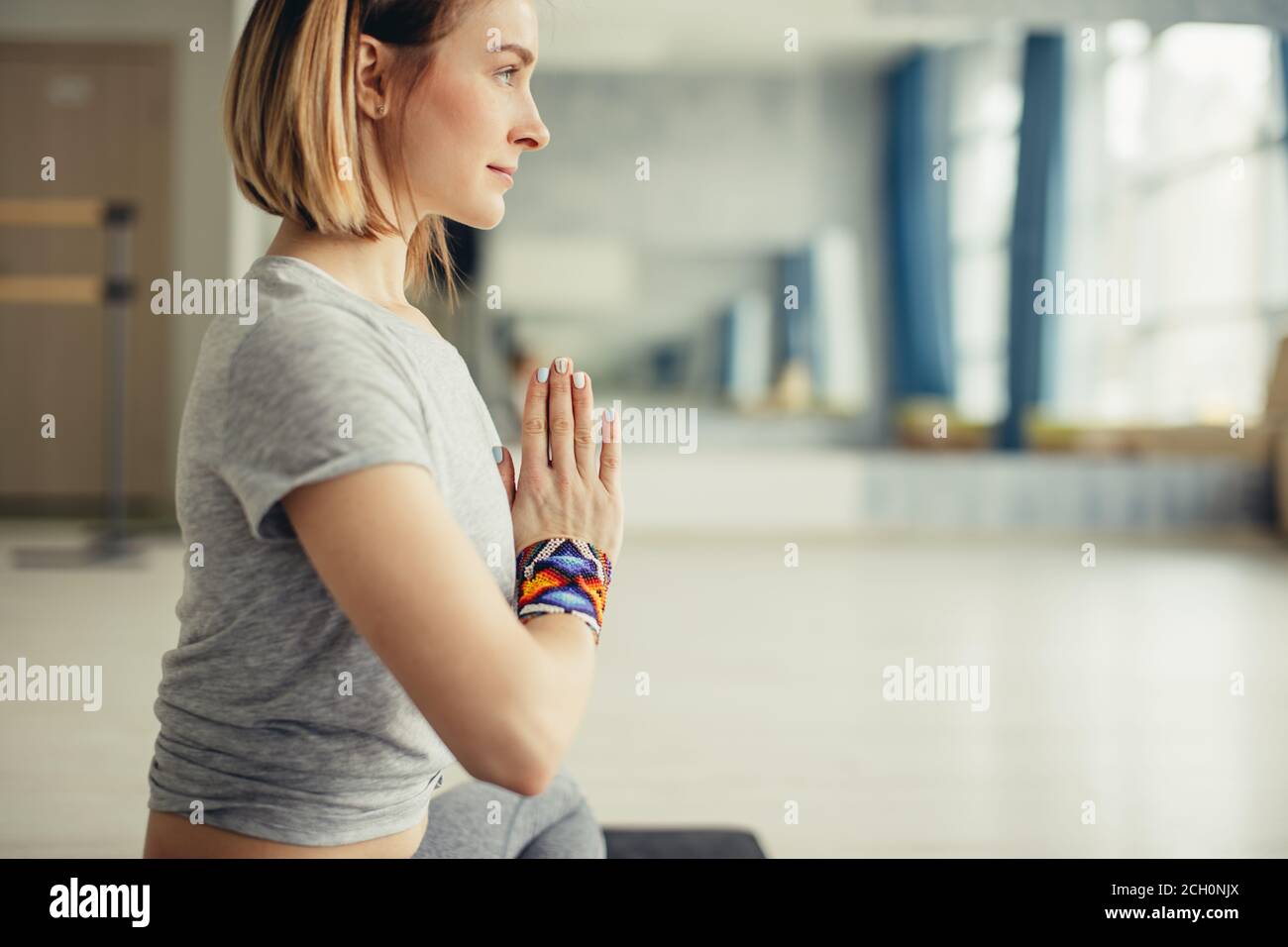 Practicing yoga sitting in padmasana. Young woman in lotus pose doing breathing exercise on mat at sport club interior, copy space Stock Photo